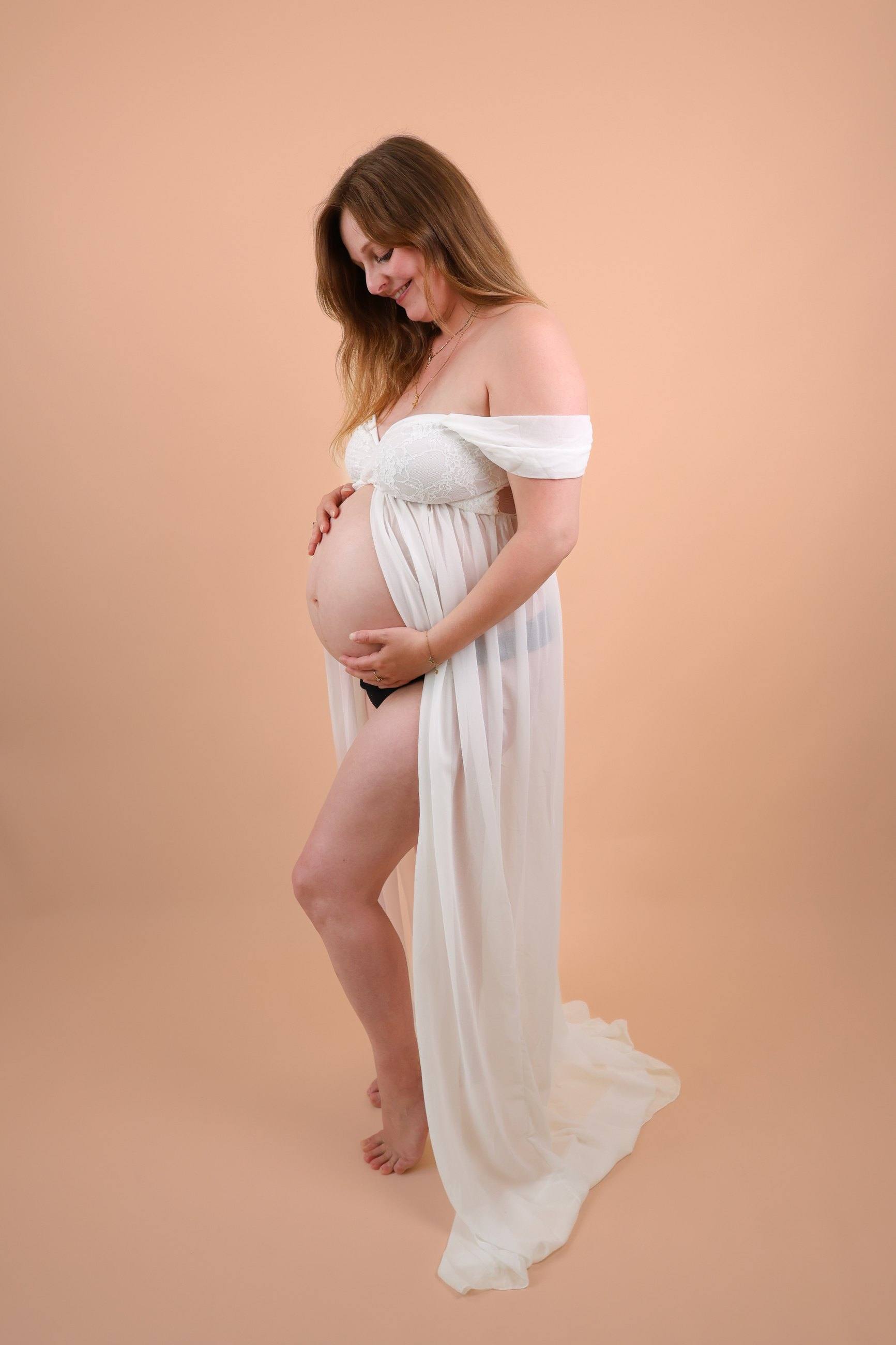 Femme enceinte en robe blanche au studio, sur fond pêche